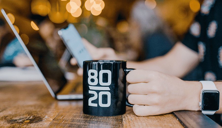 Business woman sitting in a table holding a black mug with 80/20 text design