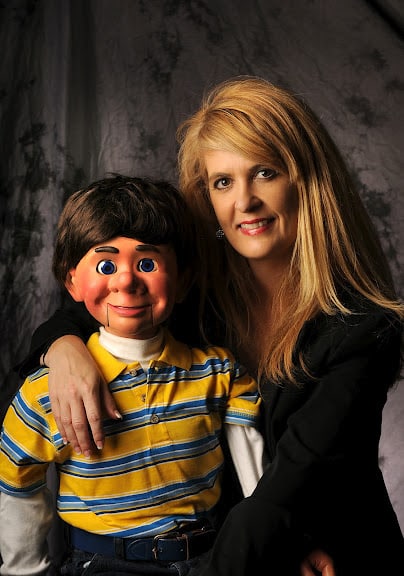woman poses with a creepy looking ventriloquist doll.