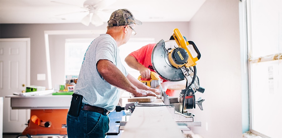 Two men in t-shirts using saws and working together on a house flipping project in a sunny, bright room