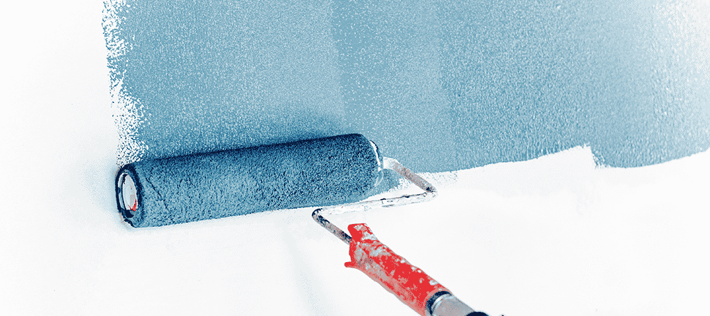 A paint roller spreading blue paint on a white wall
