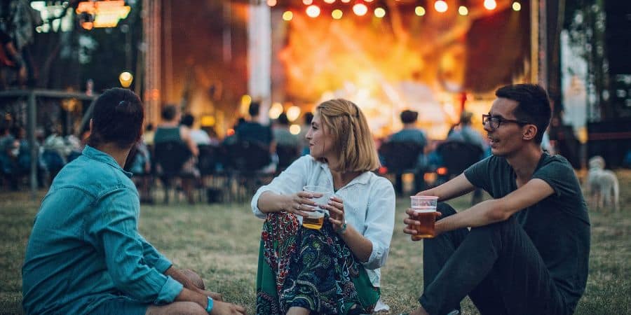 three people sitting on the ground drinking alcohol while watching festival concert