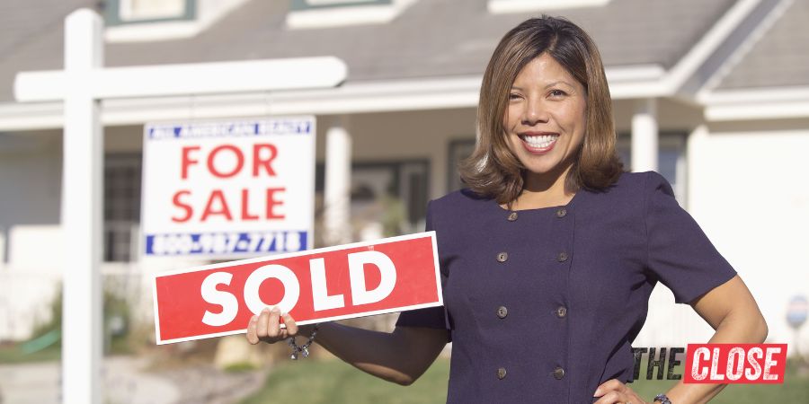 real estate agent holding a "sold" sign in front of a house with a for sale sign.