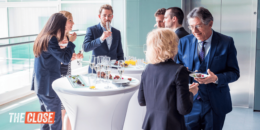 Some people dressed in professional attire standing around at an event with champagne glasses and small plates of food