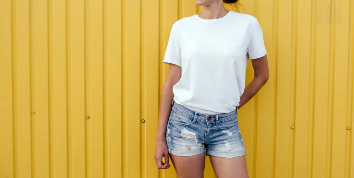 Young woman in blank white t-shirt near color background on street wearing shorts
