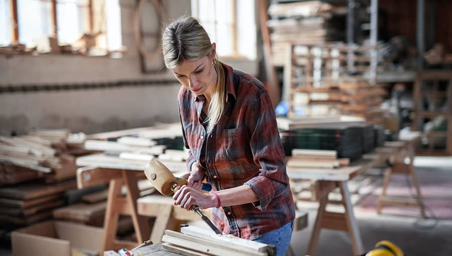 Blonde woman with a drill in a workshop, sanding down a piece of wood.