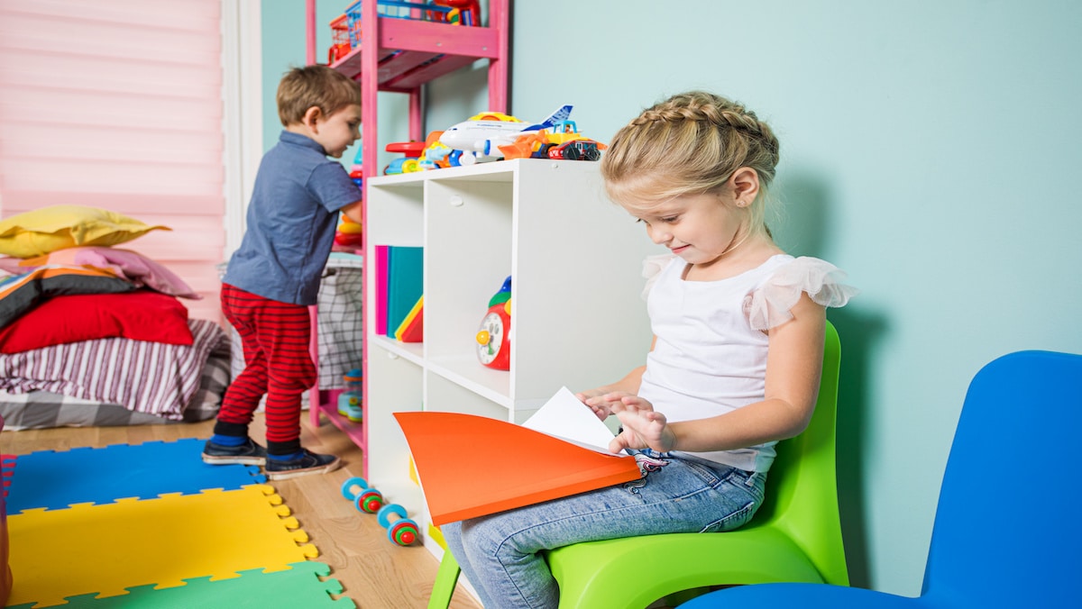 two children playing in an area with some coloring books and shelving with kid's toys.