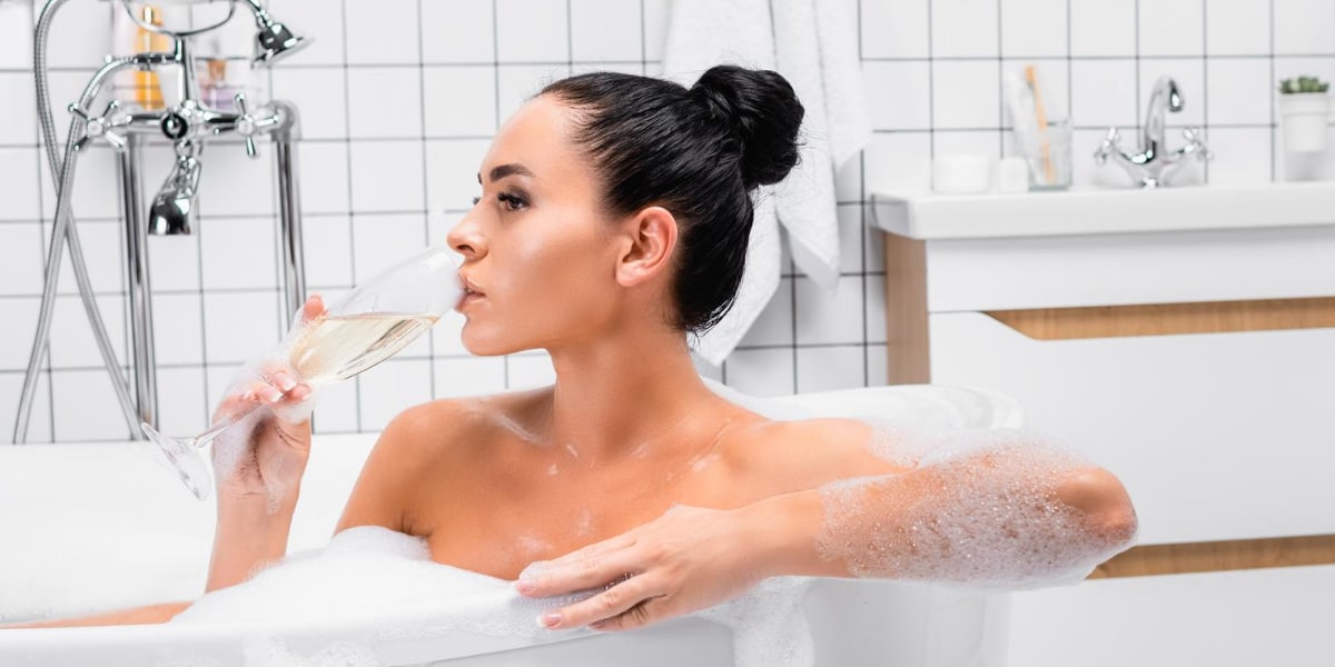 A woman drinking champagne from a bubble bath