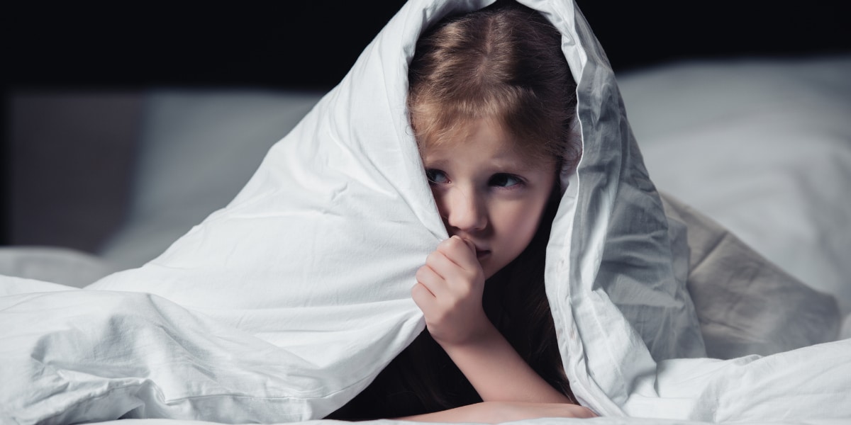 A child hiding under a bed blanket.