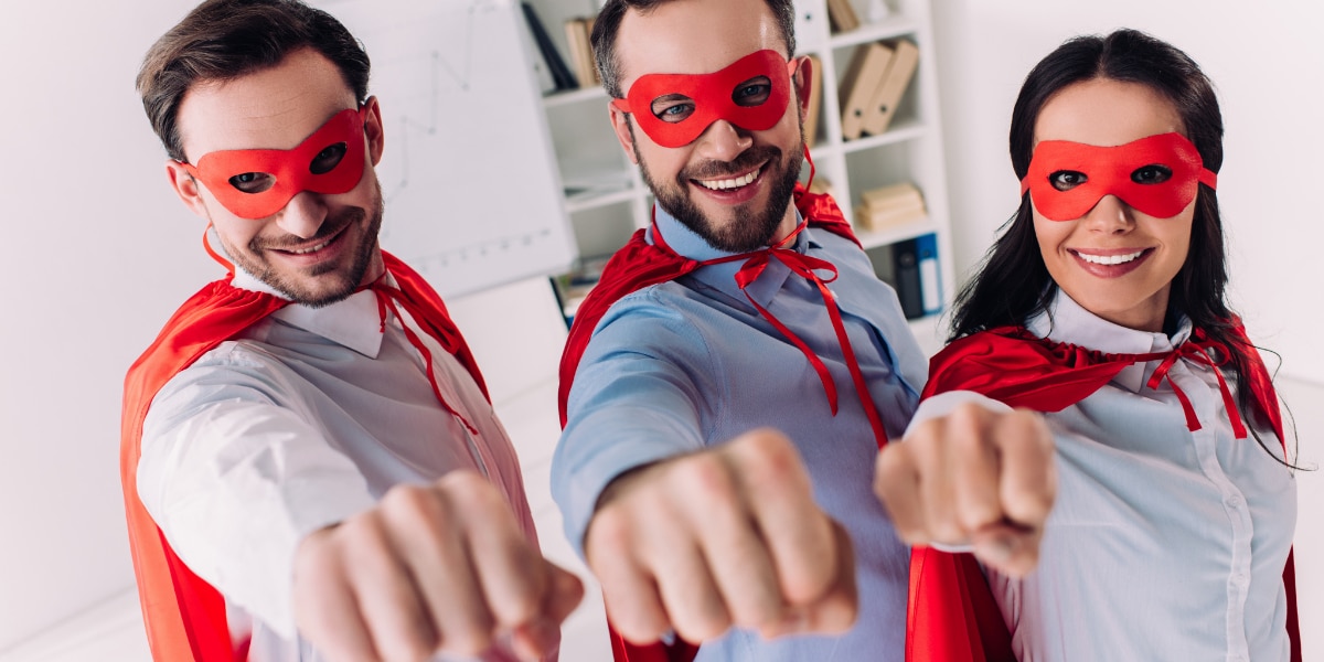 Two men and a woman wearing red eye masks and capes, pointing their fists straight forward.