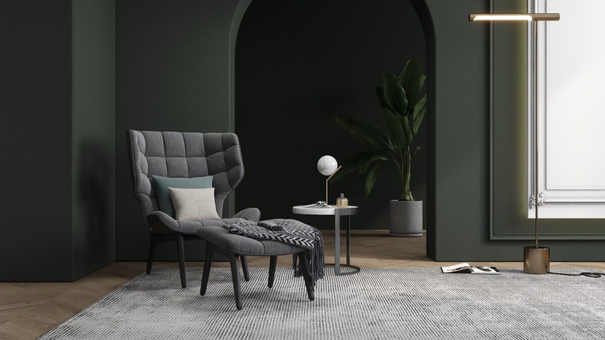 a modern chair is set against an interior design trend  moody green-gray painted wall with a potted plant in the background.