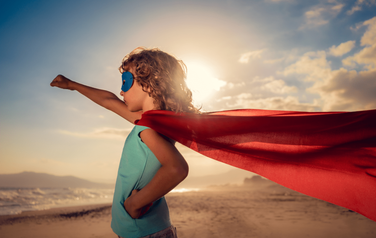 Young girl standing with her arm outstretched, wearing a red superhero cape.