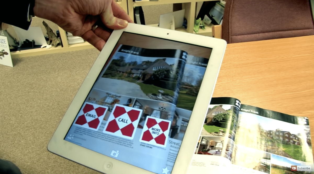 Man holding an iPad over a magazine to show augmented reality pop-up feature.
