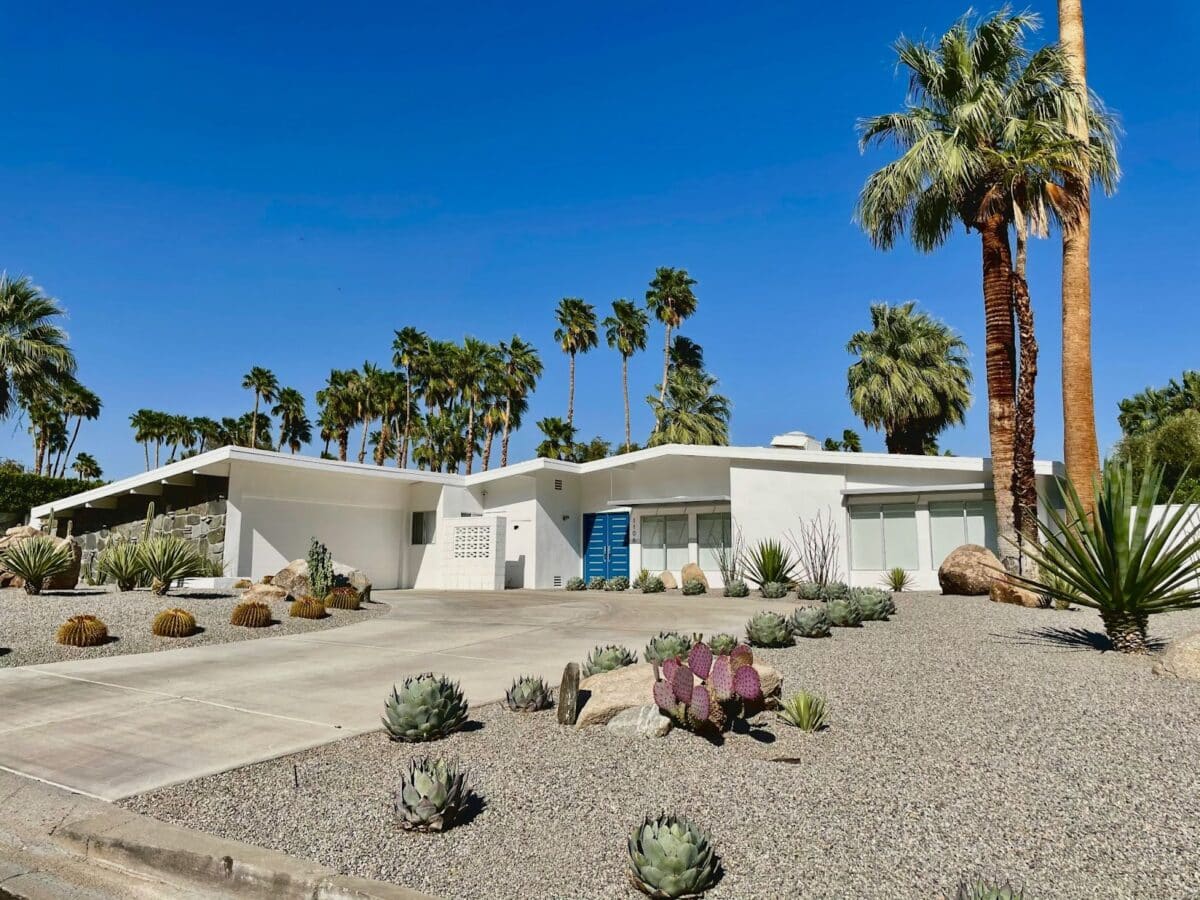 A white midcentury modern house surrounded by palm trees