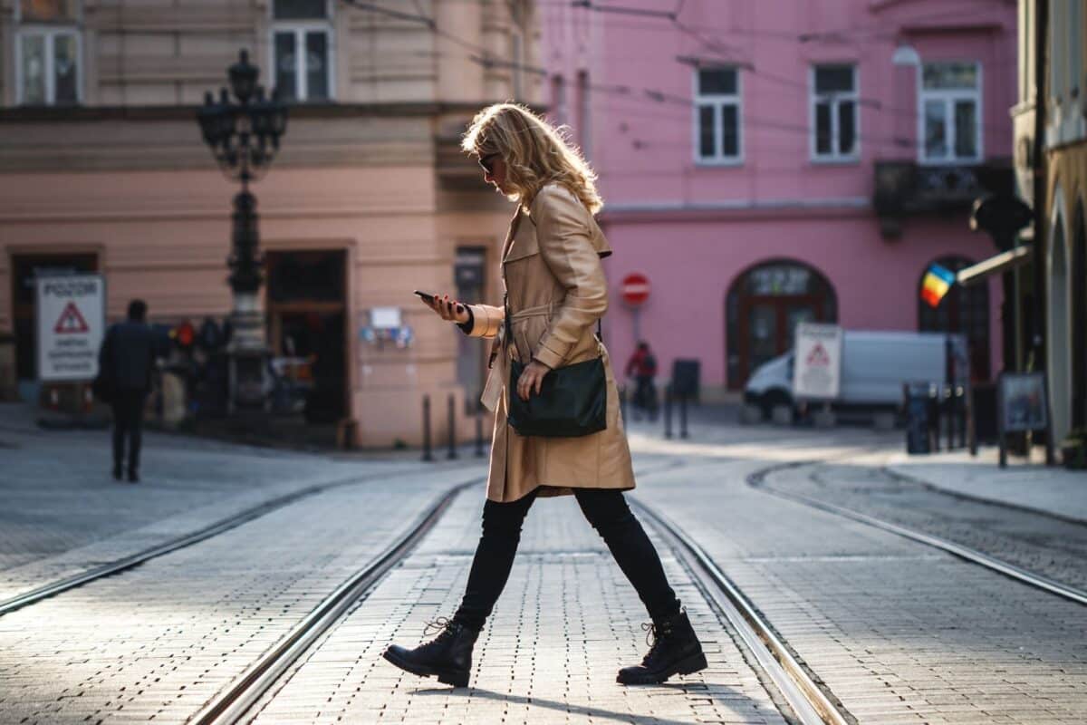 Woman walking down an urban street in the morning, checking her cell phone.