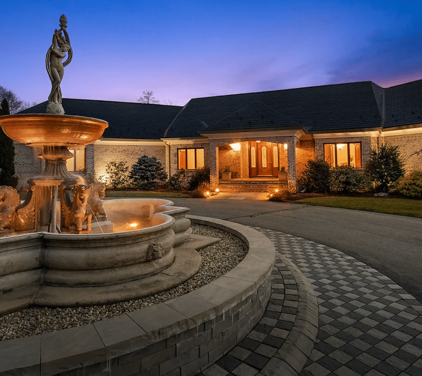 Beautiful high quality image, a brick ranch home with fountain in front during twilight hours, with blue and pink sunset behind the home.