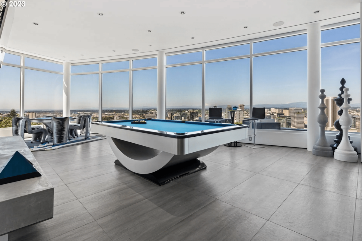 A game room with pool table and windows overlooking a skyline