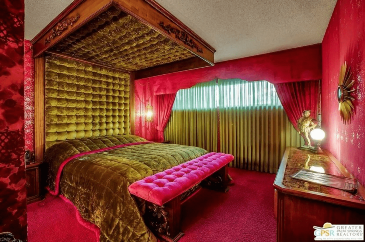 A bedroom with a bed covered in green duvet, fuchsia bench, fuchsia carpet, and fuchsia curtains