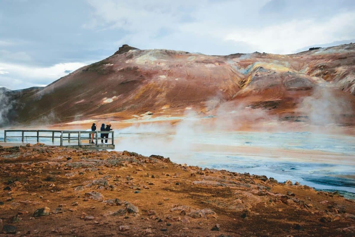 People standing on a bridge over smoky mud pools in Iceland