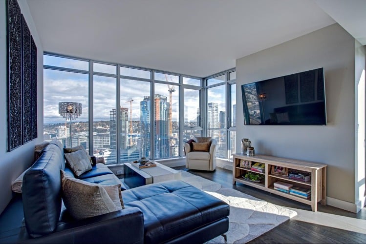 A livingroom in a staged condo with large windows overlooking a city.