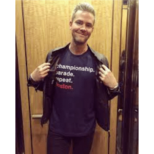 Ryan Serhant holding his jacket open to reveal a shirt that says "Champtional. Parade. Repeat. Boston."