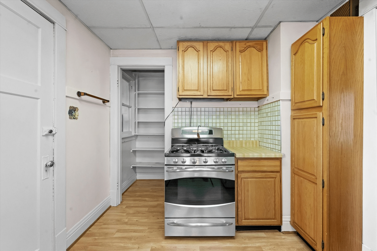 A small kitchen with a gas range, kitchen cabinets, and a small pantry in the corner