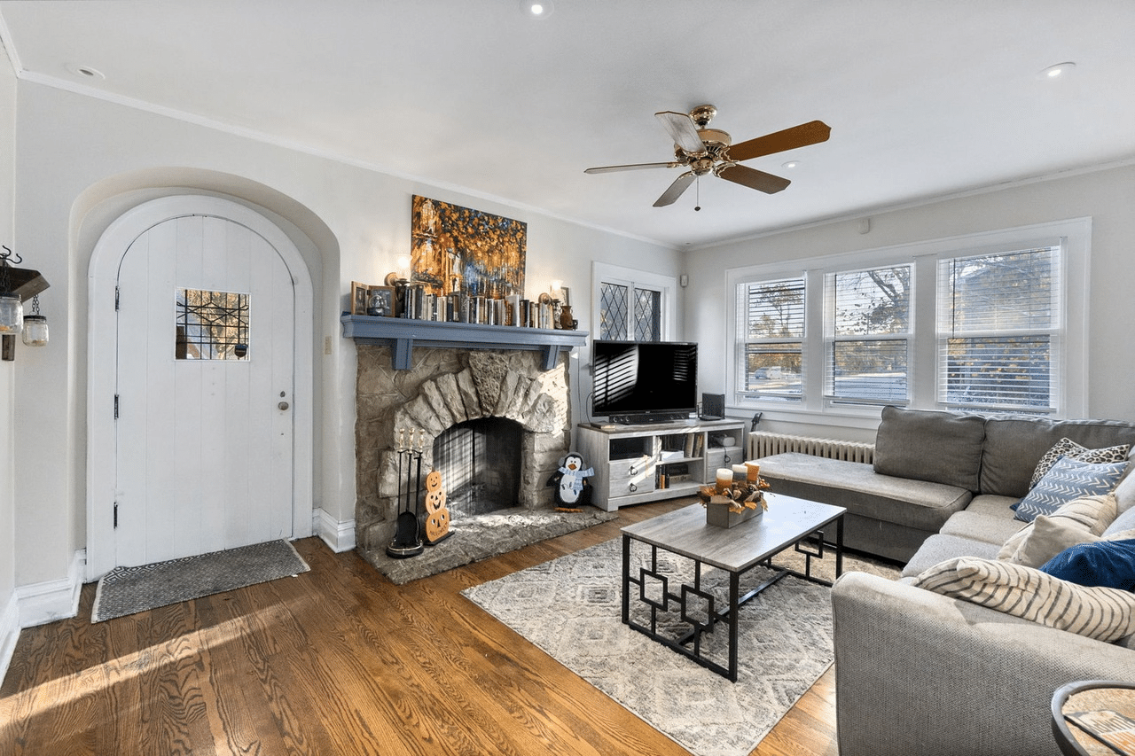A cozy living room with a stone fireplace, sofa set, television, and an arched door